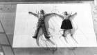 man and woman lying on their backs, "pinned" by chair bases