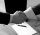 Two people shaking hands over a piece of paper with a pen on it.  Only the hands and half of each arm is visible on each person. Picture is in black and white. 