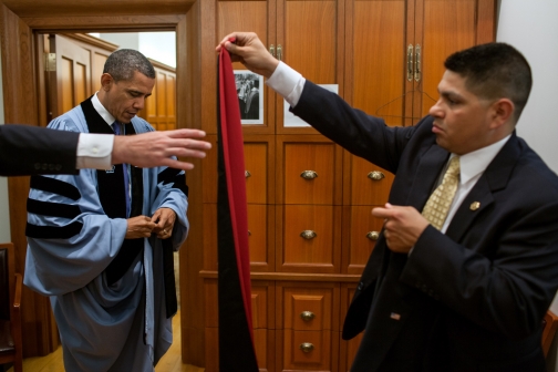 Valet Paul Reyna, right, and Trip Director Marvin Nicholson assist President Barack Obama with his academic regalia 