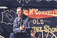 Ray Hicks telling stories in front of a medicine show banner