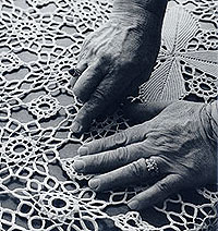 Bessie Collias's hands  pointing to a join in the lace of a crocheted tablecloth 