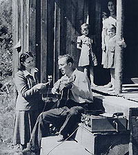 Anne Warner recording Frank Proffitt, who sings and plays the guitar, as children look on