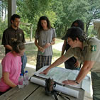 Students gathered around a forest ranger at a table looking at a map