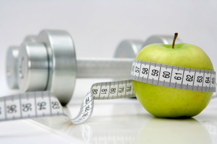 Close-up of an apple with a measuring tape around it and chrome dumbbells at the background