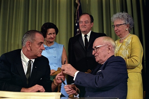 President Lyndon Johnson hands President Harry S. Truman a pen at the signing of the Medicare Bill at the Harry S. Truman Library, Independence, Missouri