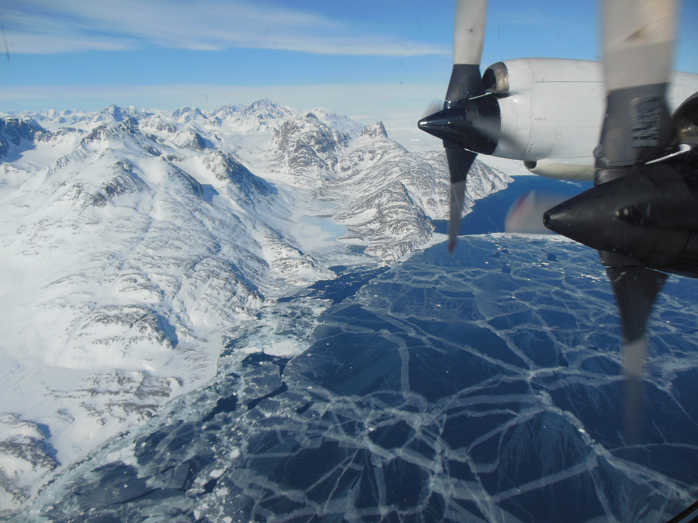 The plane flies over sea ice. The P-3B propeller can be seen out the window of the plane.