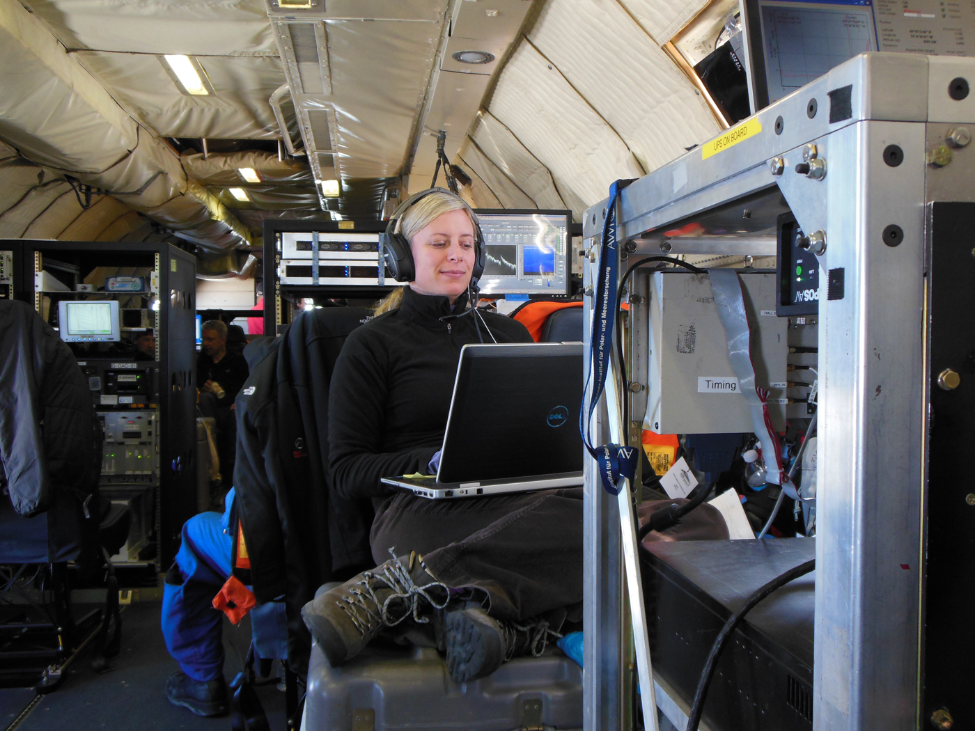 Christy Hansen sits on a toolbox while she working on the Operation IceBridge flight. She is surrounded by various scientific instruments.