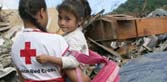 Red Cross disaster responder holding little girl in arms at tsunami disaster area