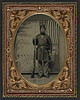[Unidentified soldier in Union uniform and forage cap with bayoneted musket in front of painted backdrop showing military camp and American flag] (LOC) by The Library of Congress
