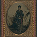 [Unidentified soldier in Union sergeant-major's uniform with sash standing with sword in front of painted backdrop showing military camp] (LOC)