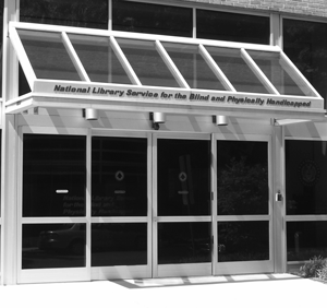 NLS Entrance: a metal and glass awning with the words “National Library Service for the Blind and Physically Handicapped” covers a set of double glass doors