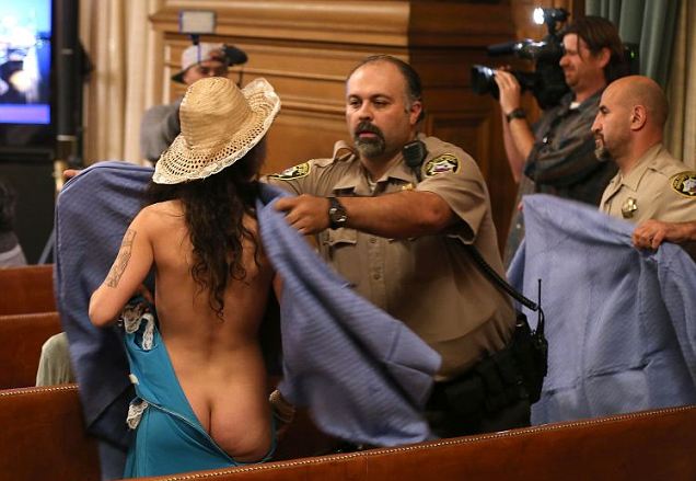 Modesty: A deputy rushes to cover a nude woman during the San Francisco Board of Supervisors meeting. She was protesting new nudity legislation in the city