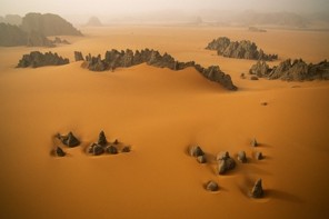 ONE TIME USE ONLY--------Pinnacles of sandstone rise through the orange dunes of the Karnasai Valley, a few kilometers from Chad’s border with Libya. The orange sand is formed by the erosion of Nubian Sandstone, which itself was formed from ancient sand dunes millions of years ago. Thus the sand is being recycled, from dune to rock to sand and back to dune again. Strong Harmattan winds sandblast the base of the sandstone pinnacles, and beautiful wind pits around their bases. This is one of the most remote parts of the Sahara. Except for one or two families of goat herders who come here once a year, it is uninhabited and otherworldly. (George Steinmetz)