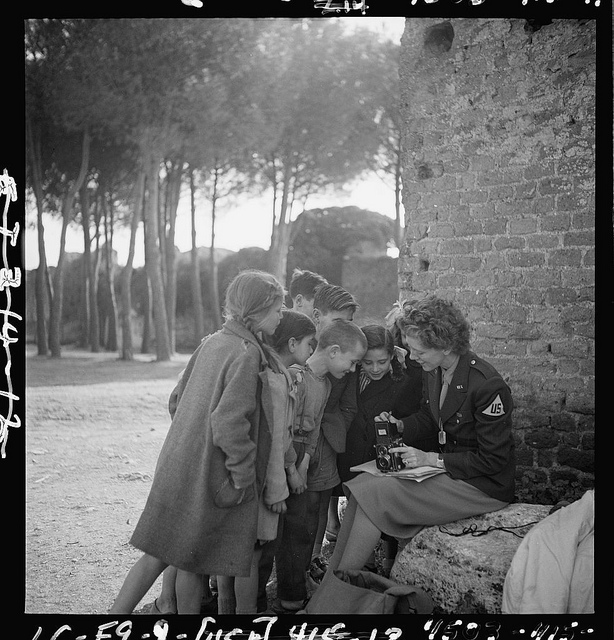 [Toni Frissell, sitting, holding camera on her lap, with several children standing around her, somewhere in Europe] (LOC)