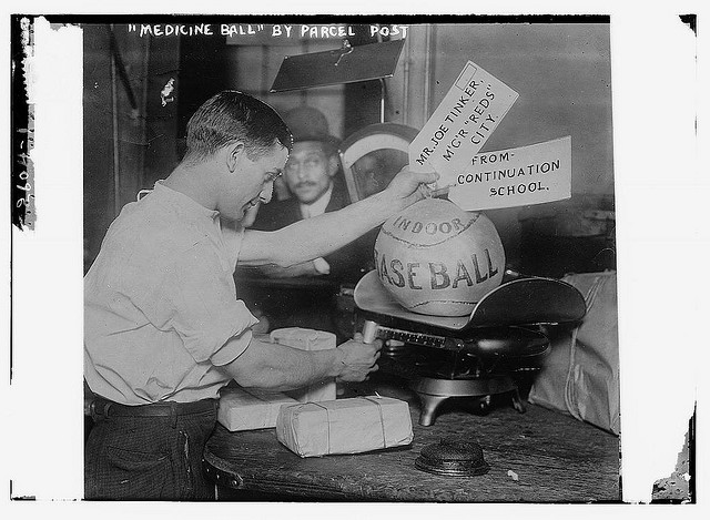 Medicine ball being weighed by Post Office employee; shipping tags read:  Mr. Joe Tinker, Mgr Reds (Cincinnati) From Continuation School.  [1913] (LOC)
