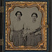 [Sisters Lucretia Electa and Louisa Ellen Crossett in identical skirts, blouses, and jewelry with weaving shuttles] (LOC)