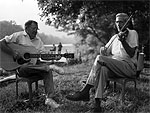Two men seated under a tree, playing their instruments