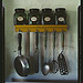 [Kitchen utensils hanging below a spice rack with mint, caraway, thyme, and sage jars] (LOC)
