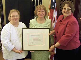 Photo of Karen Keninger, Ava Smith and Peggy Rudd hold large award plaque.
