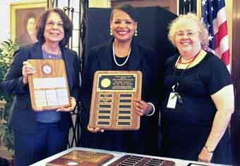 Photo of Sharon Ruda, Deborah Taylor and Carolyn Sung with array of plaques.