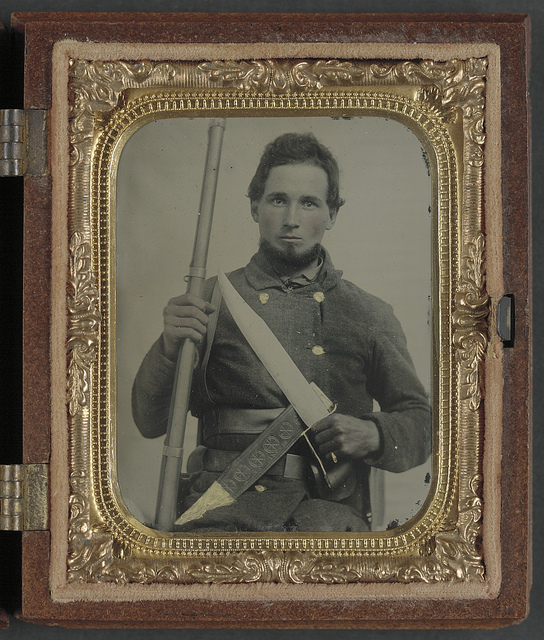 [Unidentified soldier in Confederate uniform with musket, D guard Bowie knife, and knife sheath labeled Philadelphia Avengers, N.Y.] (LOC)