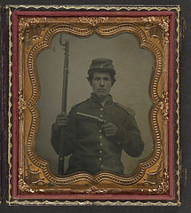 [Unidentified young soldier in Union uniform with shoulder scales and forage cap with Company I insignia holding revolver and bayoneted musket] (LOC)