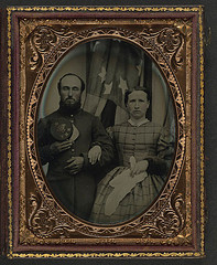 [Unidentified soldier in Union frock coat holding Company G, 12th New Hampshire Infantry Regiment forage cap next to unidentified woman in front of an American flag] (LOC)