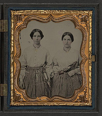 [Sisters Lucretia Electa and Louisa Ellen Crossett in identical skirts, blouses, and jewelry with weaving shuttles] (LOC)