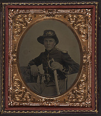 [Unidentified soldier in Union uniform with gauntlets, shoulder scales, and cavalry Company K Hardee hat holding dual Colt Model 1855 Root sidehammer pistols and cavalry saber] (LOC)