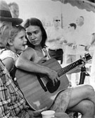 A woman playing a guitar, with a small child and elderly man watching