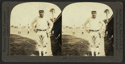 George Herman "Babe" Ruth, full length, standing, facing front; wearing baseball uniform; in field with hands on hips; other players in background.