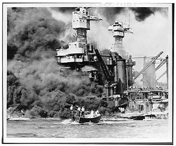 Pearl Harbor, Hawaii. A small boat rescues a seaman from the 31,800 ton USS West Virginia burning in the foreground. Smoke rolling out amidships shows where the most extensive damage occurred.