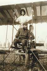 Photo: of a biplane on the ground, with pilot & passenger tied to plane with a  rope.
