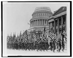 A parade of veterans carrying American flags file by the U.S. Capitol.