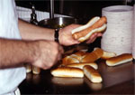 A man's hands and arms, putting wieners into buns