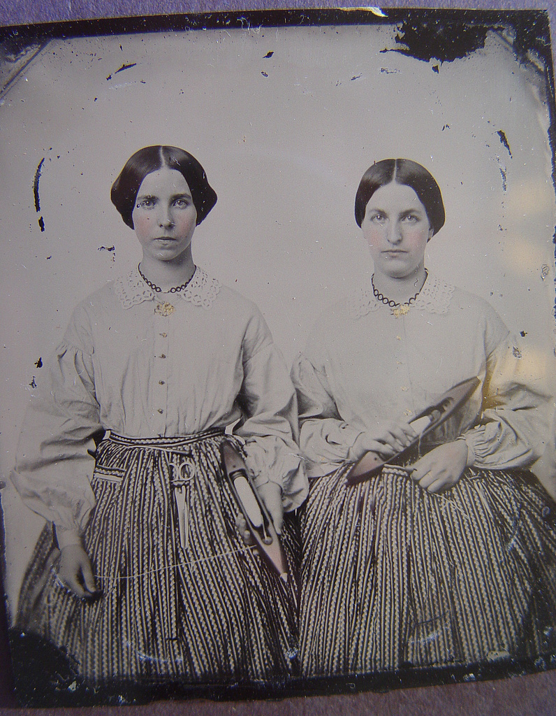 [Sisters Lucretia Electa and Louisa Ellen Crossett in identical skirts, blouses, and jewelry with weaving shuttles] 