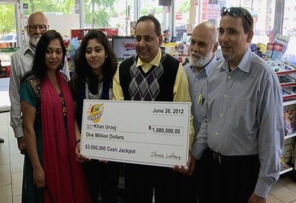 This photo provided by WMAQ-TV in Chicago shows Urooj Khan, center, holding a ceremonial check in Chicago for $1 million as winner of an Illinois instant lottery game. At left, is Khan's wife, Shabana Ansari. Khan, 46, died suddenly on July 20, just days before he was to collect his winnings. Khan's death has been ruled a homicide.