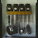 [Kitchen utensils hanging below a spice rack with mint, caraway, thyme, and sage jars]  (LOC)