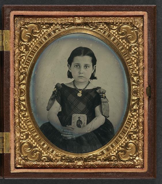 [Unidentified girl in mourning dress holding framed photograph of her father as a cavalryman with sword and Hardee hat]