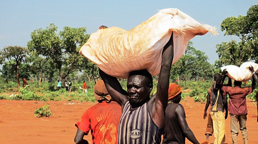 A man carries a large package of food air dropped by the World Food Program to the Yida Camp in South Sudan, October 28, 2012. [State Department photo/ Public Domain]