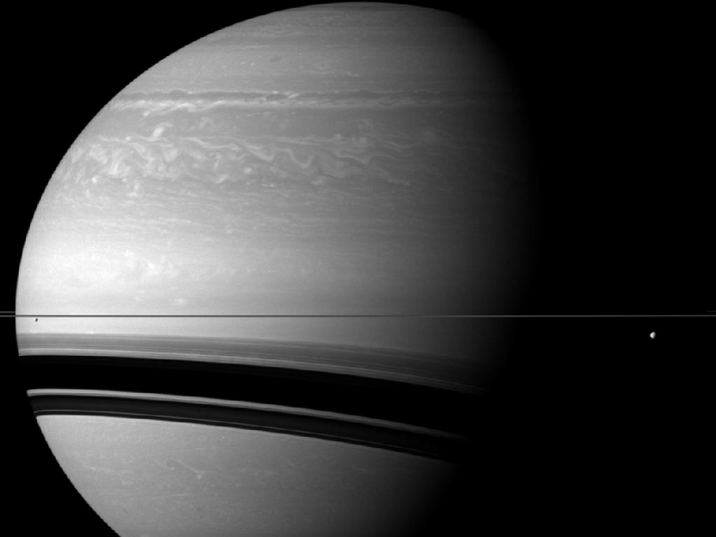 Image description: The Cassini spacecraft took this photo of Saturn in December 2011 from a distance of approximately 1.3 million miles away. The scale of the image is about 77 miles per pixel.
Three of Saturn&#8217;s moons, Tethys, Enceladus, and Pandora, are shown. Tethys is on the right of the image, below the rings. Enceladus is on the left, below the rings. Pandora is barely visible. It appears as a small grey speck above the rings on the extreme left edge of the image.
Photo from NASA/JPL-Caltech/Space Science Institute