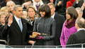 President Obama places his hand on the bible and takes his oath in front of a crowd