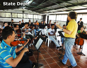 grupo de jóvenes músico tocando sentados mientras el conductor dirige de pie