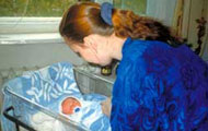 Photo Michelle Berdy/CCP, courtesy of Photoshare, a woman nurse bends over a newborn in a plastic hospital crib