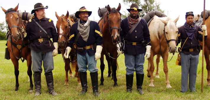 Photo of four men, dressed in 19th century military uniforms, with horses