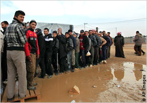 أناس يقفون في طوابير بجوار مستنقع موحل (AP Images)