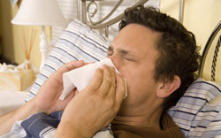 Sick man in bed blowing his nose.