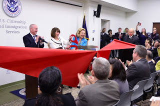 Director Mayorkas (standing left) applauds as New York District Director Andrea Quarantillo and Congresswoman Carolyn Maloney cut the ceremonial ribbon