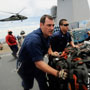 Two U.S. sailors rush humanitarian assistance supplies across the flight deck of a ship. (U.S. Navy) 