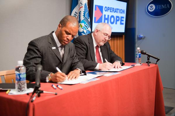 Operation HOPE Founder and CEO John Hope Bryant (L) and FEMA Administrator Craig Fugate sign a memorandum of agreement (MOA) between the two organizations.